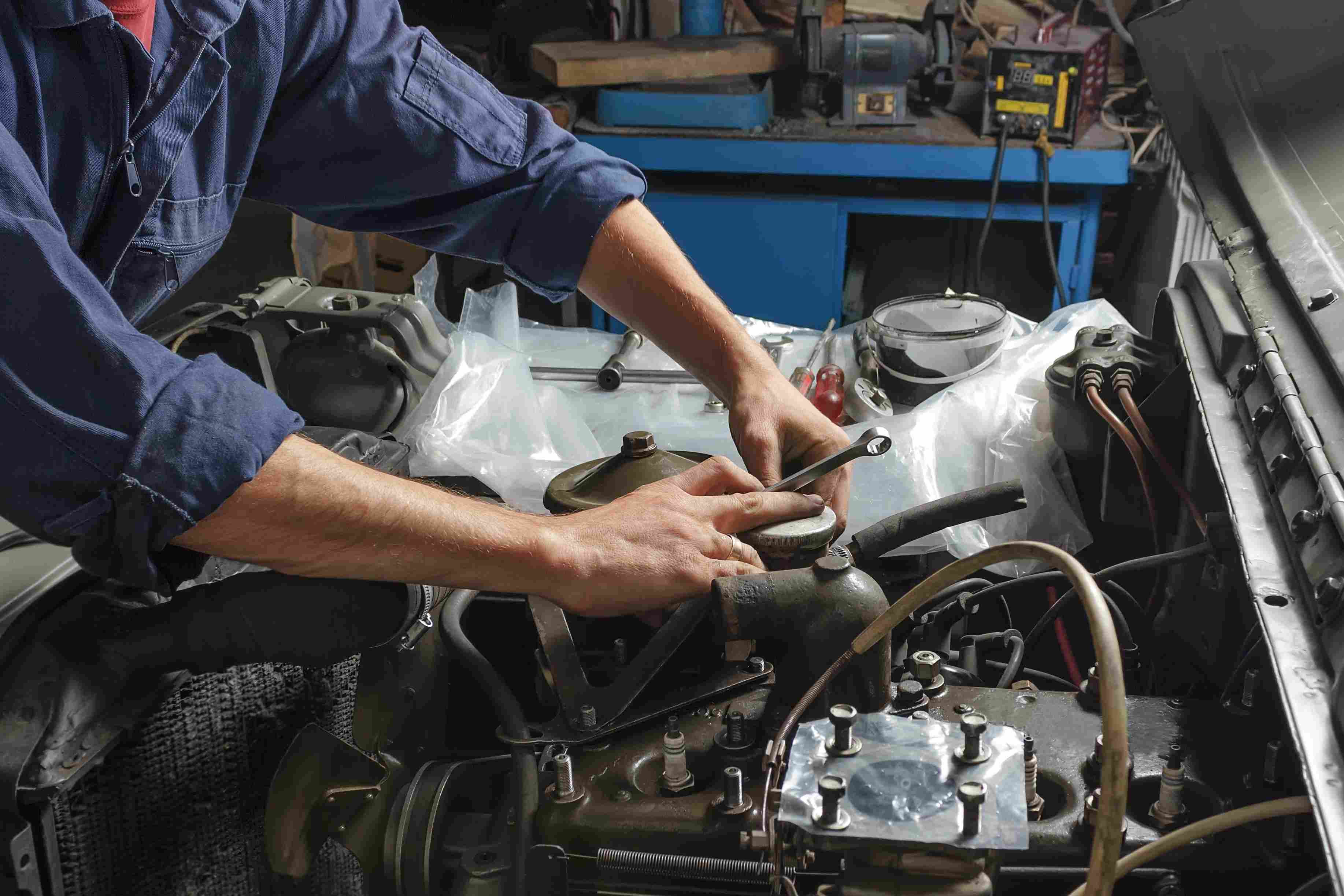 Auto mechanic working under the hood of an old car engine.